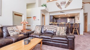 A spacious living area with a leather sofa, wooden coffee table, and a kitchen in the background. - Snowcreek #856, Updated 2 Bedrm + Loft Townhme in Snowcreek Phase 5 (Mammoth Lakes)