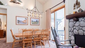 A dining area with a wooden table and chairs, a hanging light fixture, and a stone fireplace. - Snowcreek #856, Updated 2 Bedrm + Loft Townhme in Snowcreek Phase 5 (Mammoth Lakes)