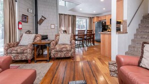 A spacious living area with a wooden floor, a dining table with chairs, a sofa, and a staircase leading to a kitchen area. - Sierra Park Villas #66, Updated 1 bedroom + 2 lofts / 2 bath, sleeps 6, free town shuttle stop! (Mammoth Lakes)