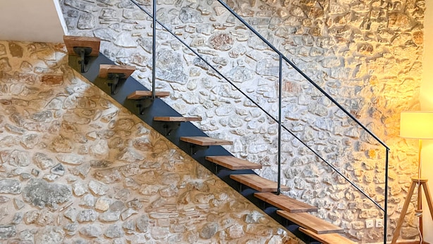 Una scala con gradini in legno e ringhiere in metallo, addossata a un muro di pietra strutturato.