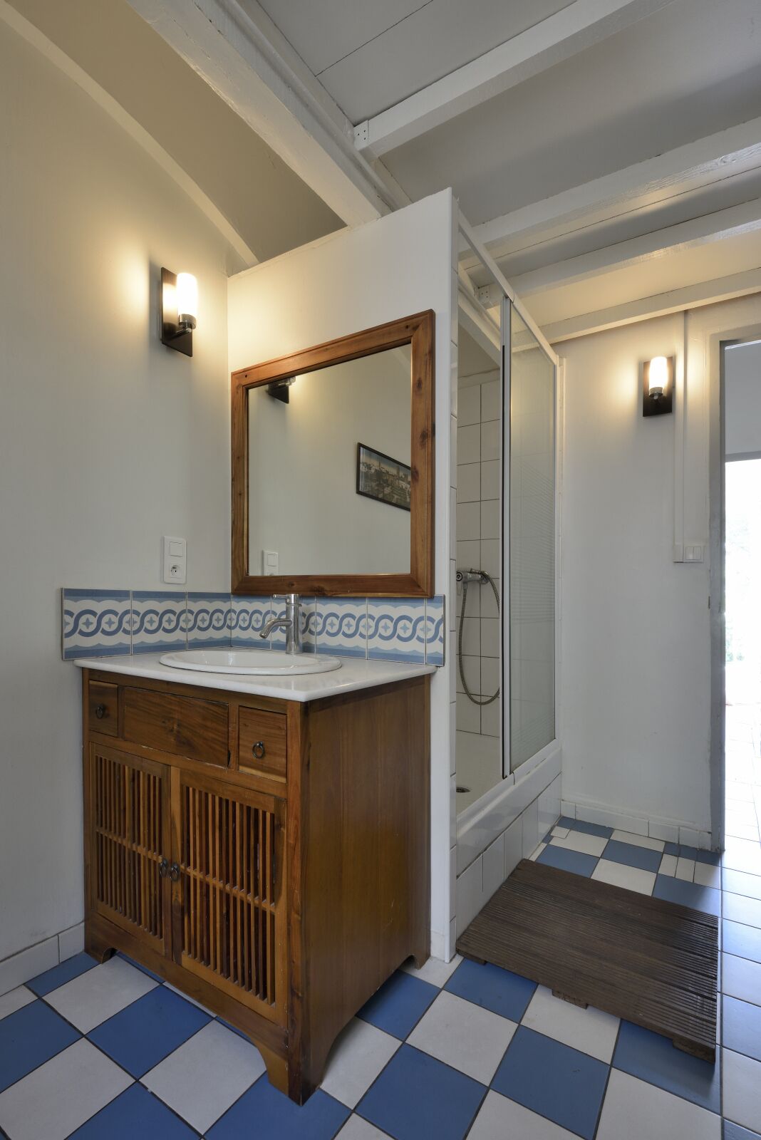 A bathroom with a wooden vanity, a large mirror, a sink, and a shower area.