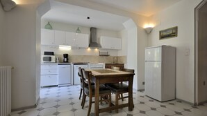 Cozinha compacta com armários brancos, uma mesa de jantar com cadeiras, geladeira e micro-ondas.