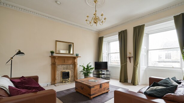 A living room with a fireplace, a television, and a large window with curtains. - Spacious 3BR New Town Apartment (Edinburgh)