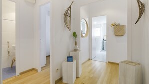 Un pasillo con suelo de madera, paredes blancas, una puerta blanca y una pequeña mesa con un florero y un cartel.