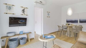 Una sala de estar moderna con un televisor de pantalla plana, un comedor con sillas de mimbre y un cuadro abstracto grande.