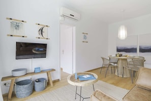 A modern living room with a flat-screen TV, a dining area with wicker chairs, and a large abstract painting.