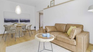 Una sala de estar moderna con un sofá color crema, una mesa de centro redonda, sillas de mimbre, una lámpara colgante y un cuadro en la pared.
