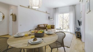 Un comedor con una mesa redonda de madera, sillas de mimbre, un sofá y un balcón con vistas.