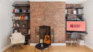 Uma sala de estar com lareira de tijolos, estantes de livros, televisão e um violão.