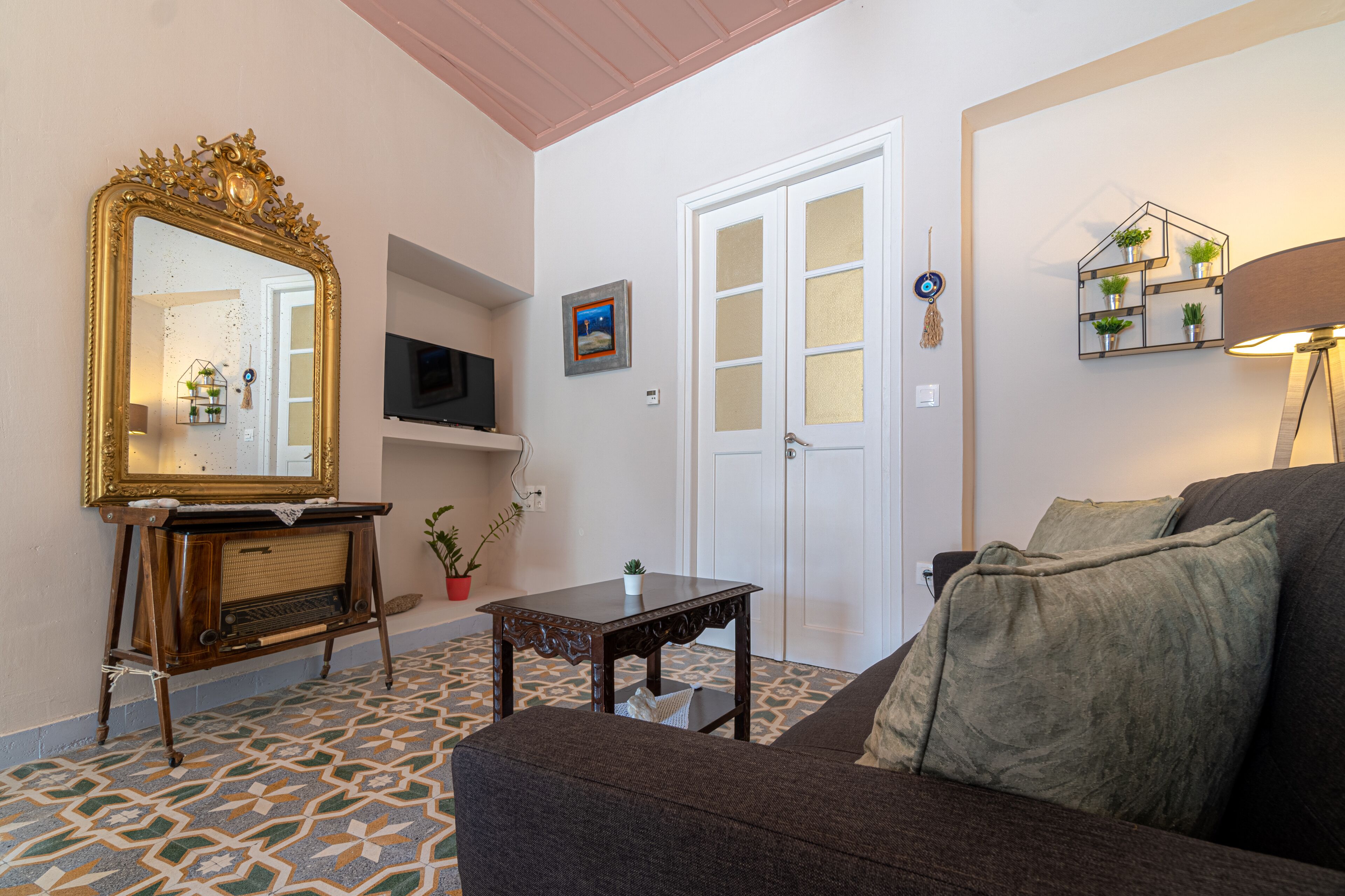 Ein Wohnzimmer mit einer Couch, einem Couchtisch, einem Fernseher, einem dekorativen Spiegel und einer Tür mit Wanddekoration in geometrischem Design.