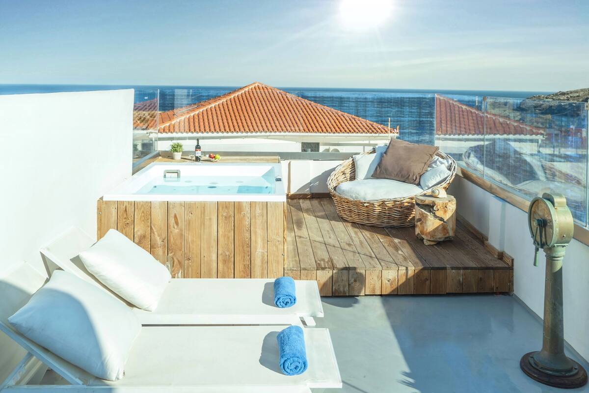 A rooftop terrace with a hot tub, lounge chairs, and a view of the sea.