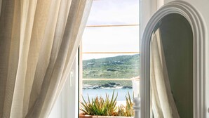 Vista da janela com cortinas, uma planta em vaso e um vislumbre da paisagem.
