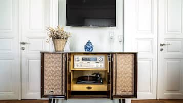 Una habitación con un mueble de madera que contiene una radio antigua, un jarrón con flores secas y un televisor colgado en la pared.