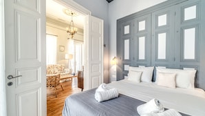 Quarto de hotel com uma cama grande, duas toalhas sobre a cama, piso de madeira, uma escrivaninha com cadeira e um candelabro.