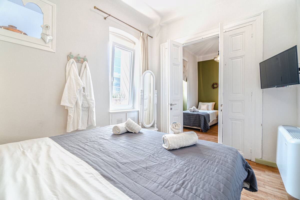 A bedroom with a bed, a mirror, a TV, and a door leading to another room.