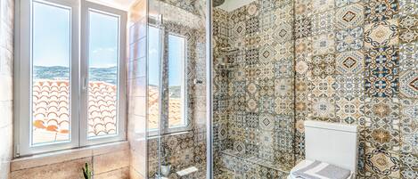 A bathroom with a shower, a toilet, and a window with a view of the sea.