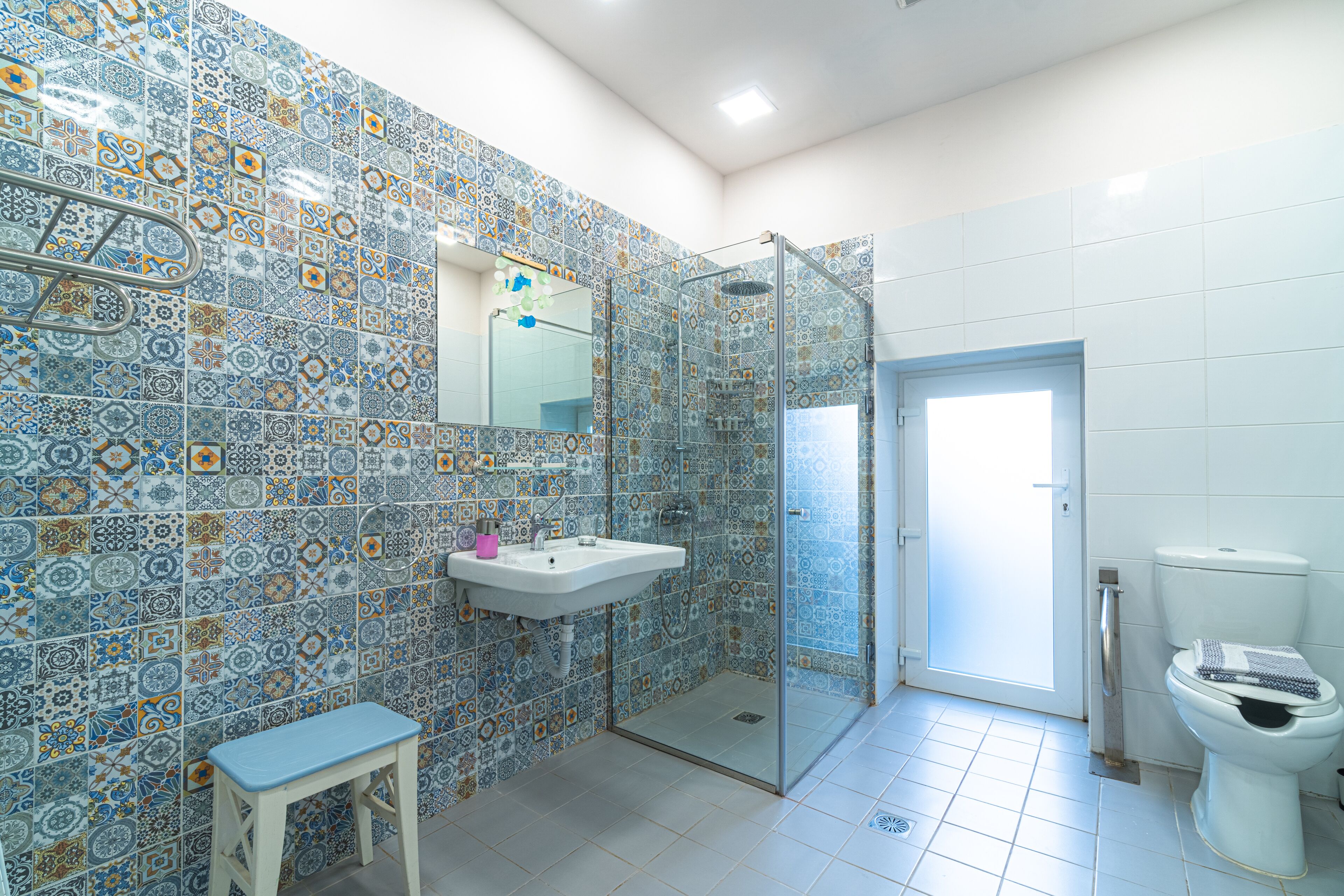 A bathroom with patterned tiles, a glass shower enclosure, a sink, and a toilet.
