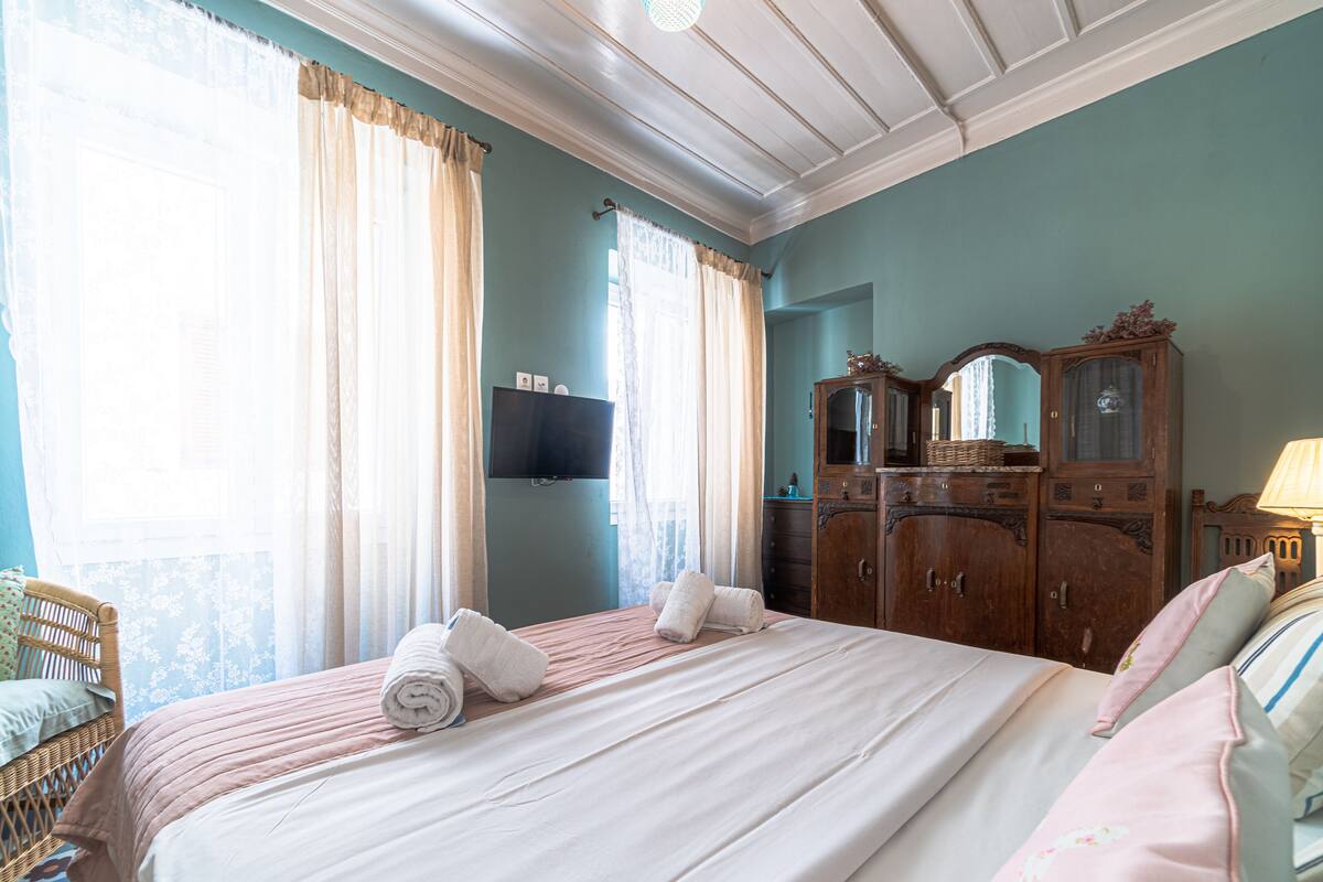 A bedroom with a bed, curtains, a dresser, a television, and a lamp.