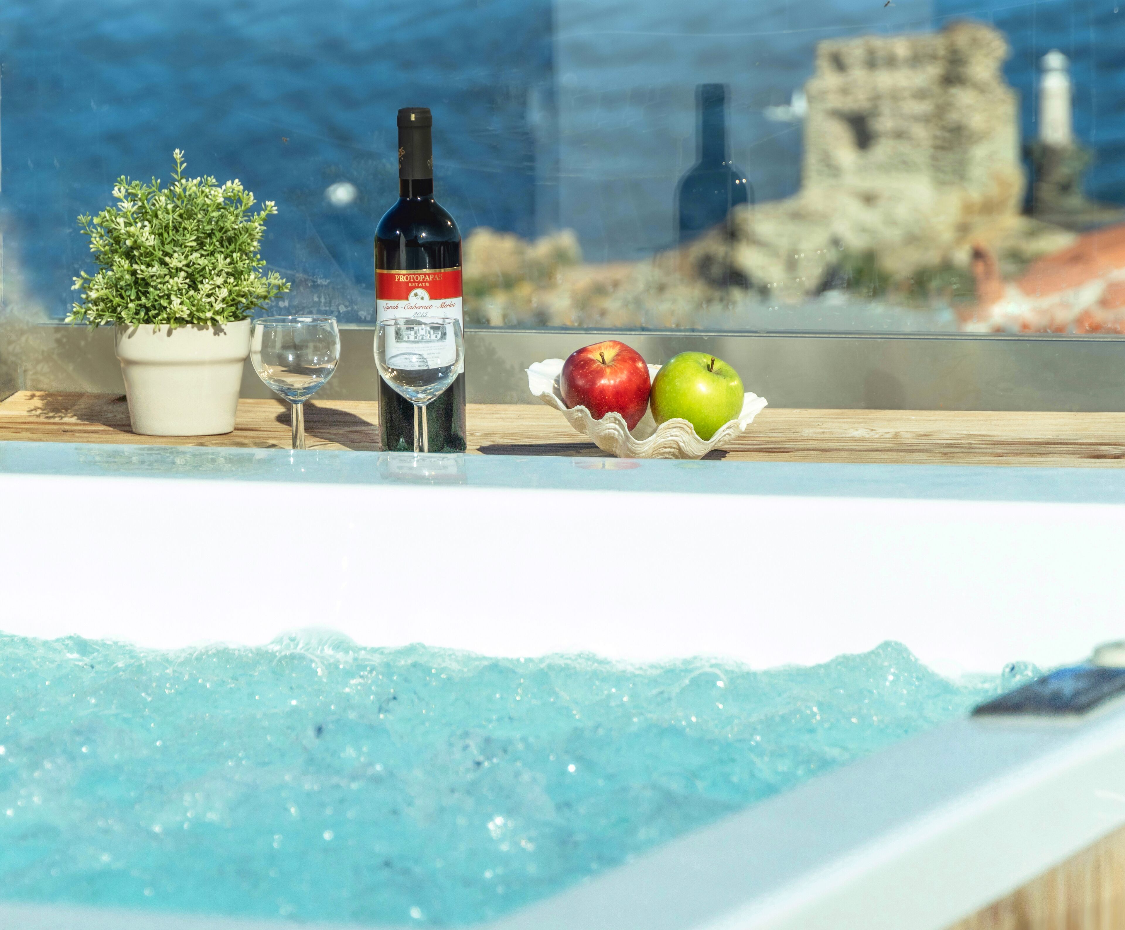 Un tavolo in vetro con una bottiglia di vino, un bicchiere e una ciotola di mele.