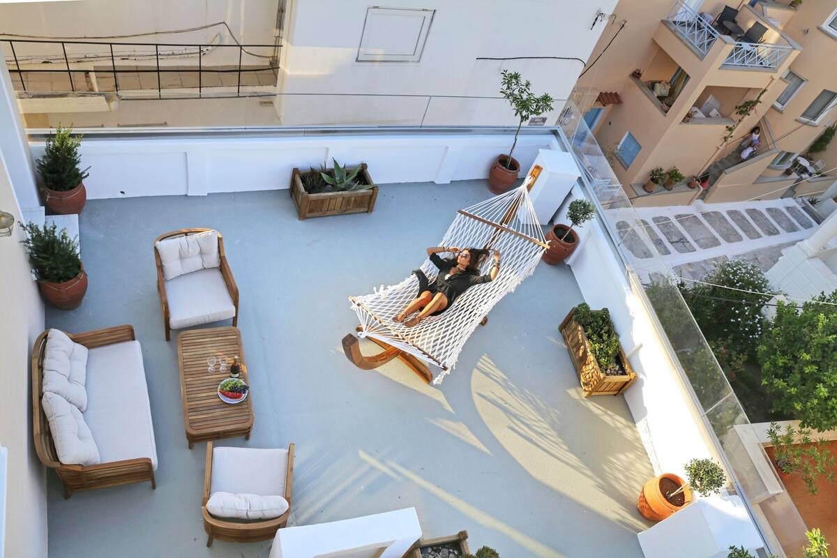 A rooftop terrace with a hammock, wooden furniture, and potted plants.