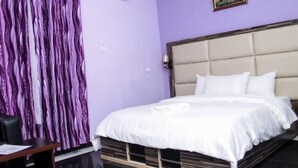 A bedroom with a bed, a desk, and a curtain. - Demeg Hotel And Suites (Lagos)
