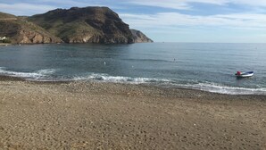 Ein Strand mit einem felsigen Hügel im Hintergrund, einem kleinen Boot auf dem Wasser und einem Kiesufer.