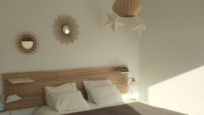 Ein Schlafzimmer mit hölzernem Kopfteil, weißer Bettwäsche, einer braunen Tagesdecke, einem Nachttisch mit Lampe und einem Wandspiegel.