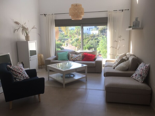 Sala de estar com sofá, poltrona, mesa de centro, armário e vista para o verde lá fora.