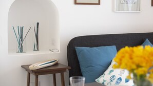 A modern room with a grey sofa, a small wooden side table, and a wall-mounted shelf with drinking straws. - La Casa di Nonno Mario (Praiano)