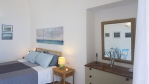 A bedroom with a bed, bedside table, lamp, and a large mirror reflecting a dining area. - La Casa di Nonno Mario (Praiano)