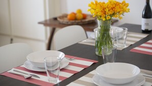 A dining table set with plates, glasses, and cutlery, a vase with yellow flowers, and a bottle of wine. - La Casa di Nonno Mario (Praiano)