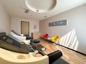 Une chambre moderne équipée d’un fauteuil de massage, d’une petite table avec des chaises et d’un tableau au mur.