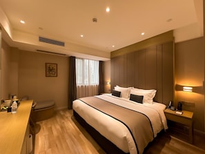 Une chambre d’hôtel avec un grand lit, des tables de chevet, un bureau et une fenêtre avec des rideaux.