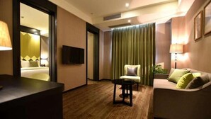 A hotel room with a wooden floor, a sofa, a chair, a desk, a TV, and a bed with a green curtain. - Shanghai Deco Hotel (SHANGHAI)