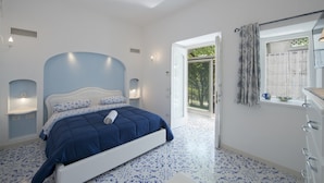 Quarto com cama, janela com cortinas e porta que dá para o exterior.