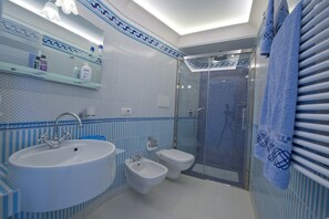A bathroom with a large sink, bidet, toilet, and a shower area.