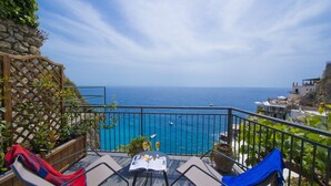 Uma varanda com vista para o mar, uma mesa com uma revista e um copo, e duas cadeiras de descanso.