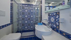 Casa de banho com chuveiro, sanita e lavatório, destacando azulejos com padrão azul e branco.