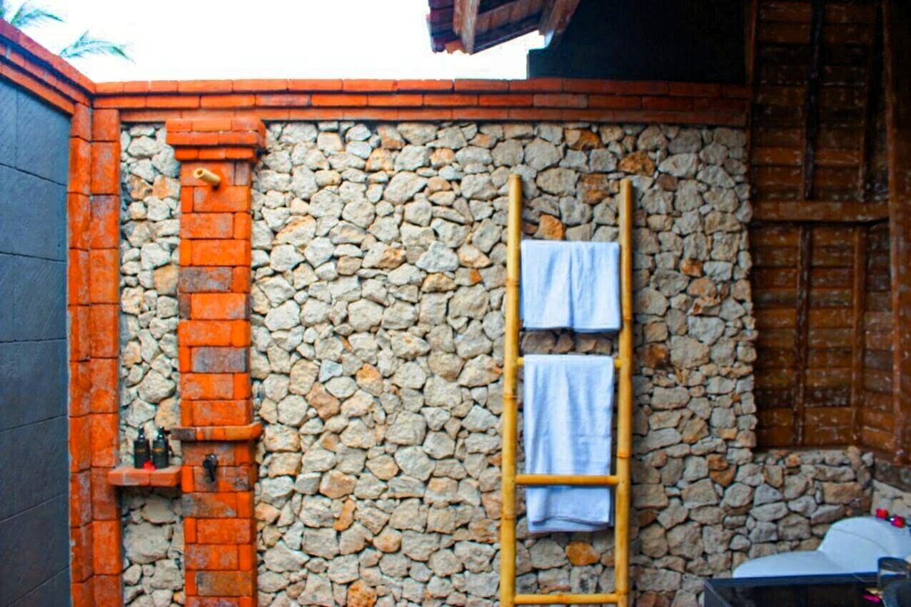 Een stenen muur met een houten ladder en handdoeken, een bakstenen muur met een plank waarop flessen staan, en een houten deur.