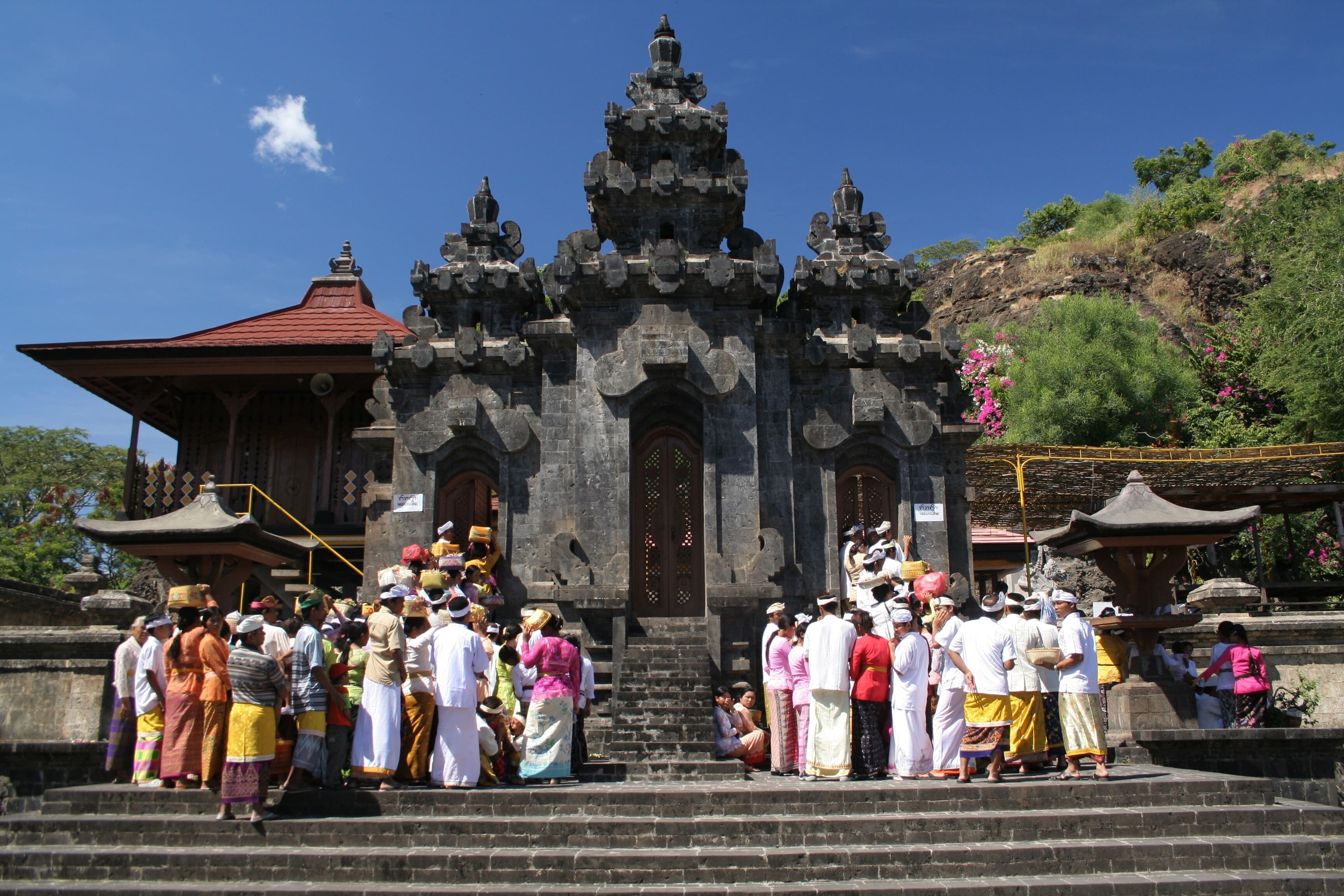 A temple with a red roof and stone architecture, surrounded by a crowd of people.