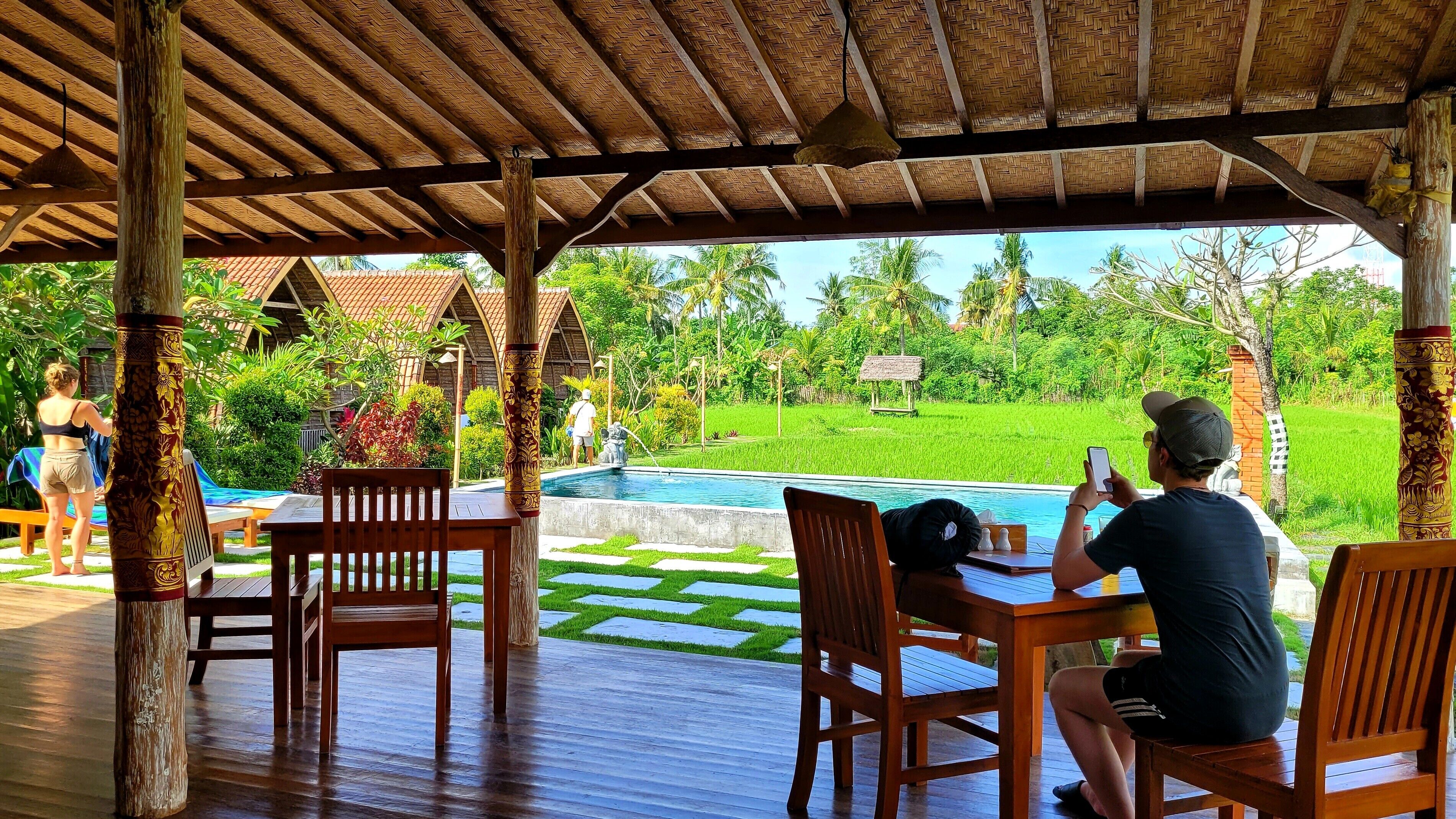 A covered outdoor area with wooden furniture and a pool.