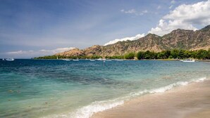 A beach with clear turquoise water, boats, and a mountainous backdrop. - Umma Bali Menjangan (Pejarakan)