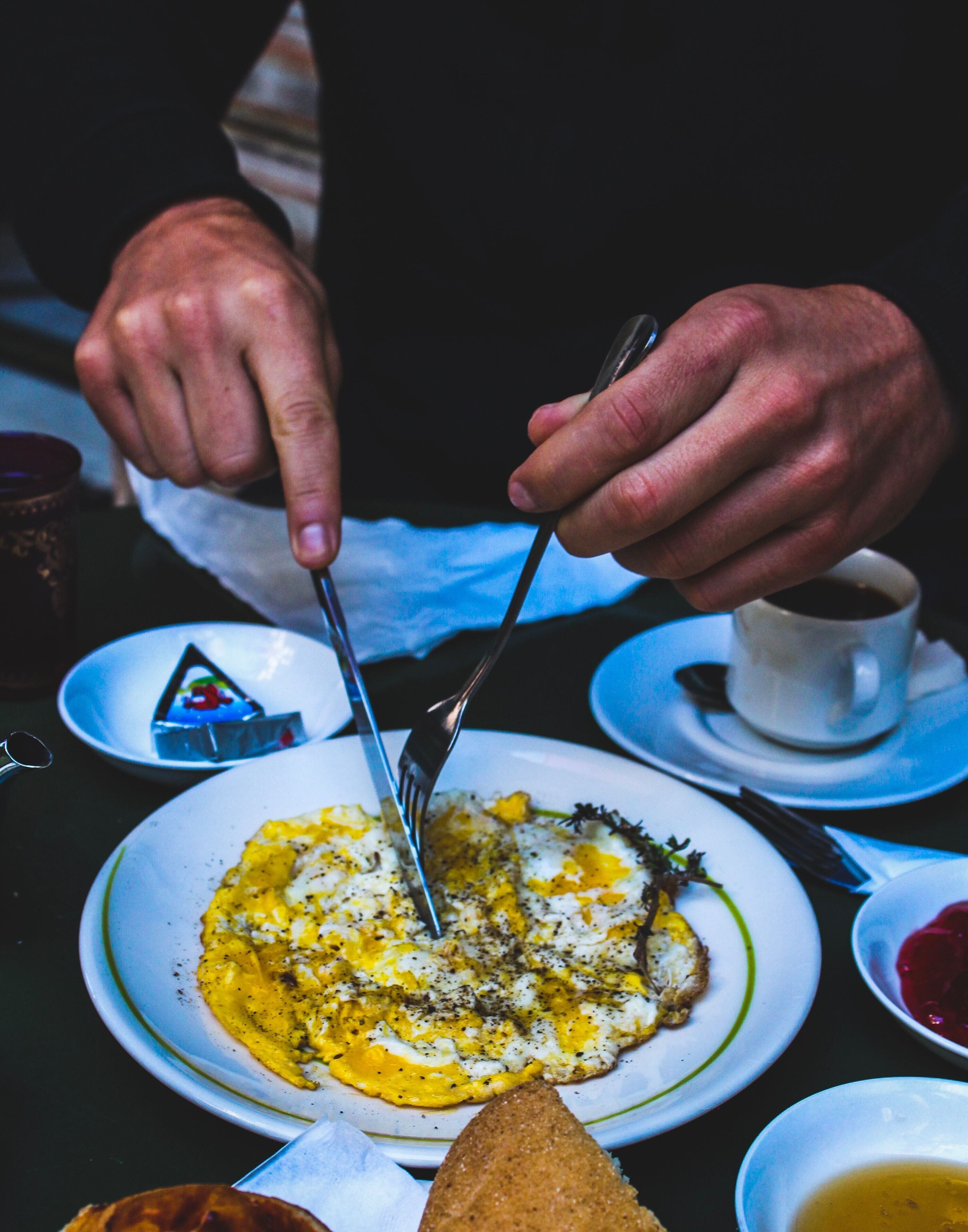 En person skærer en omelet på en tallerken med gaffel og kniv.