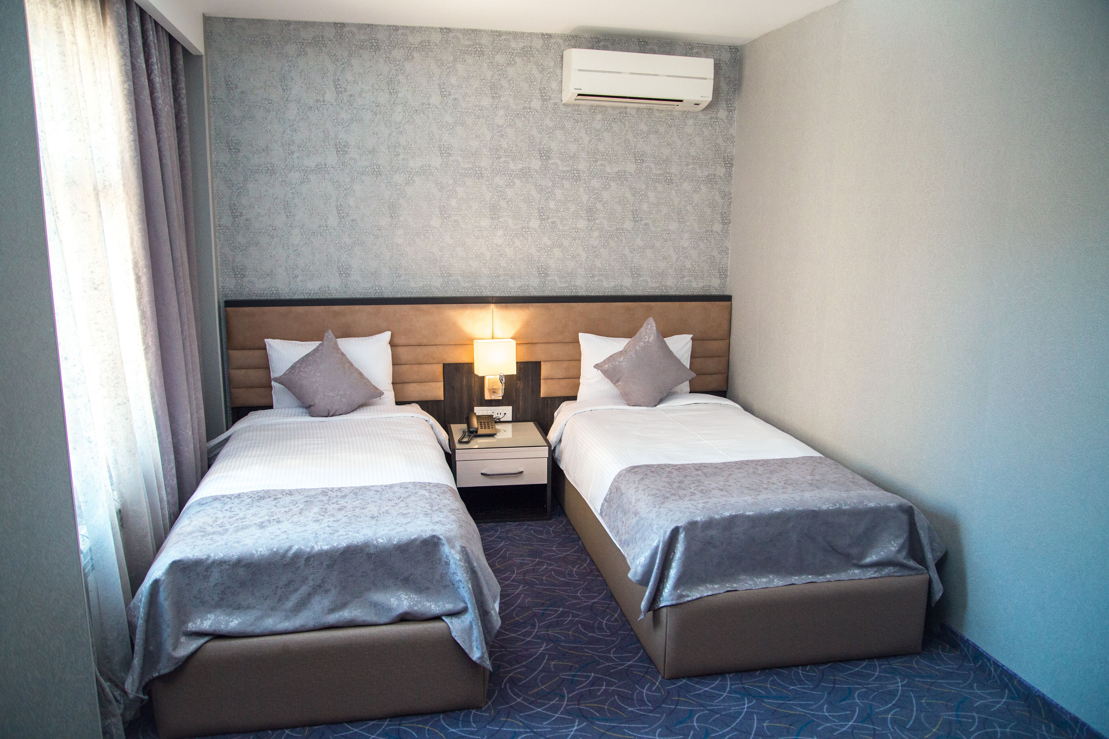 Een hotelkamer met twee bedden, een nachtkastje, een lamp en een airconditioning.