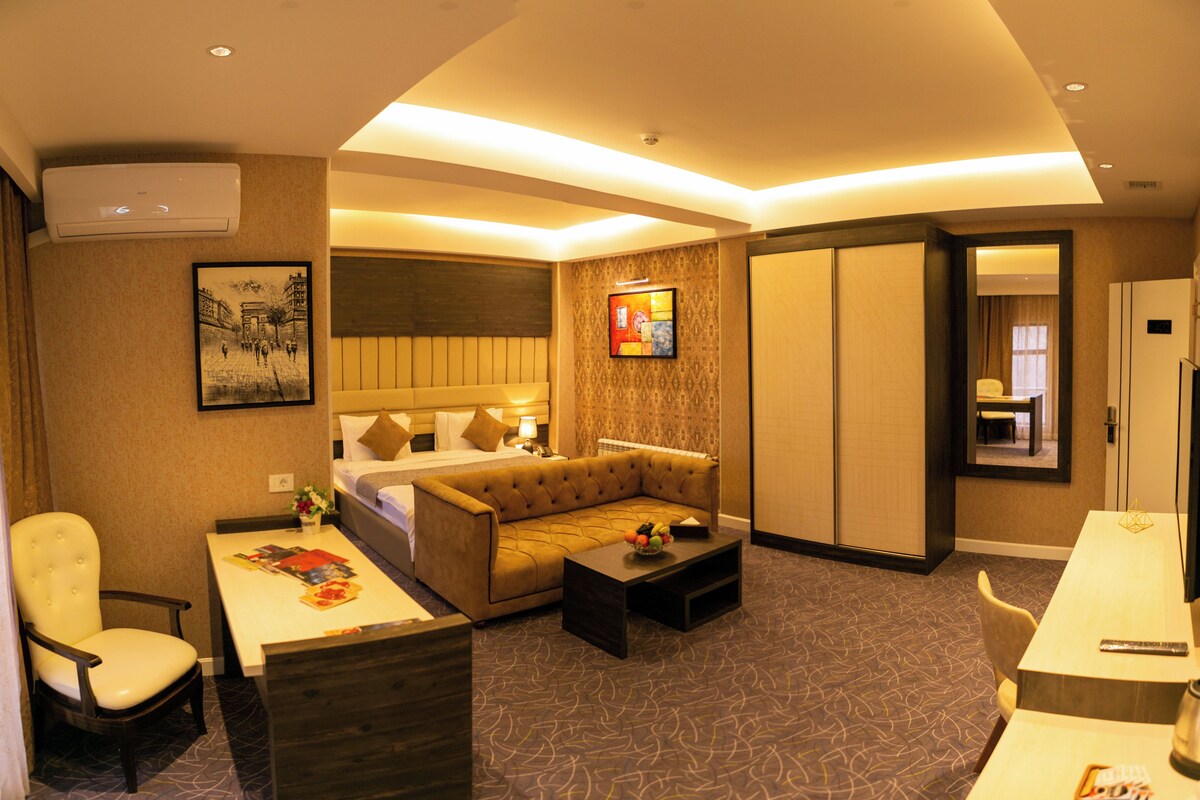 A hotel room with a bed, sofa, coffee table, and a dining table.