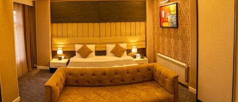 Une chambre d’hôtel avec un grand lit, deux tables de chevet avec des lampes, un canapé et un panier de fruits posé sur une table.