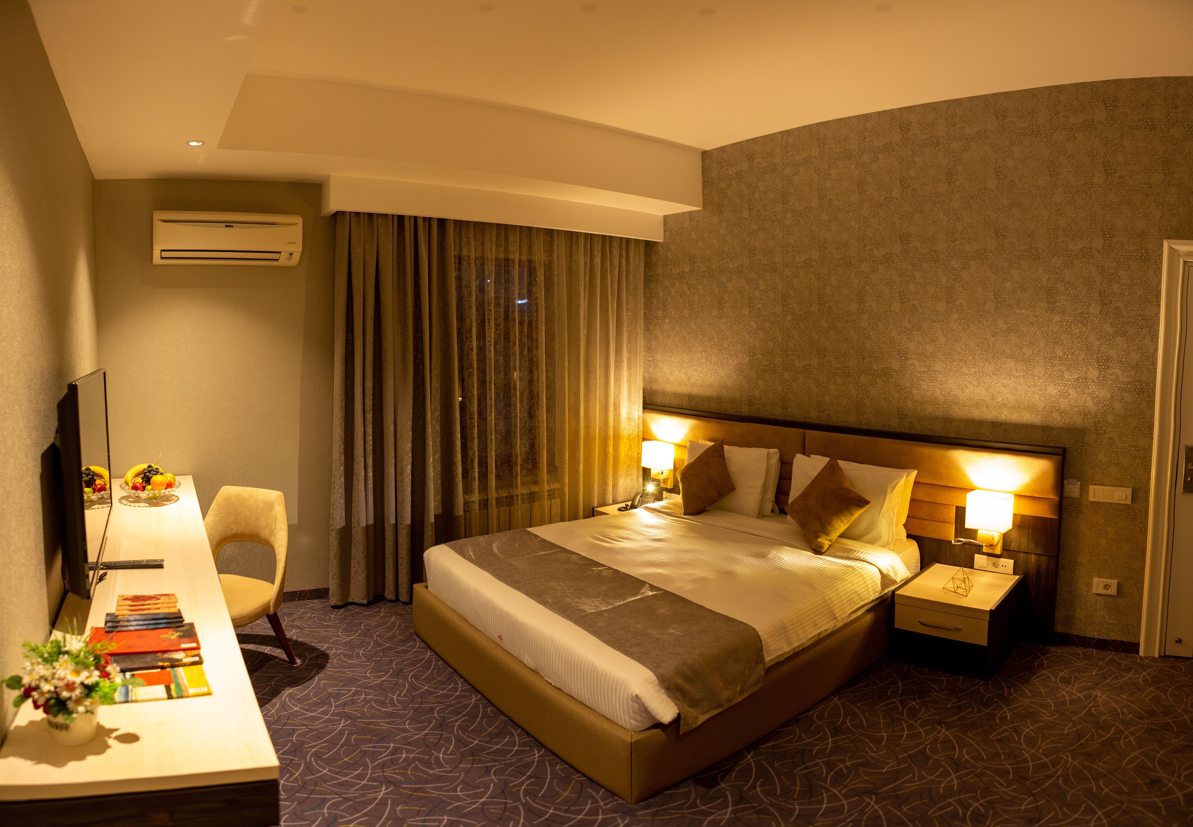 A hotel room with a large bed, bedside tables with lamps, a desk with a chair, and a TV.