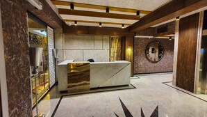 Un comptoir d’accueil au design élégant, combinant marbre et bois, une grande horloge murale et un plafond moderne doté d’un éclairage encastré.