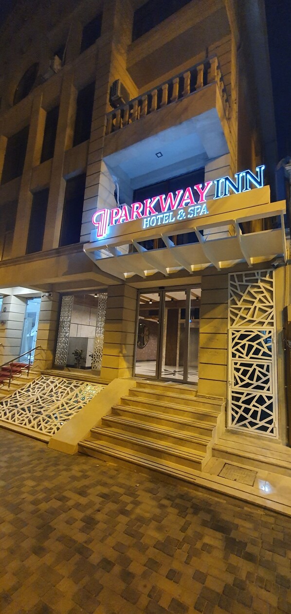 Entrada de un hotel con un letrero de neón que dice "Parkway Inn Hotel & Spa" y un juego de escaleras que conducen a la entrada.