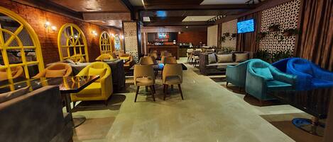 A modern lounge area with seating arrangements, a bar, and a television screen.